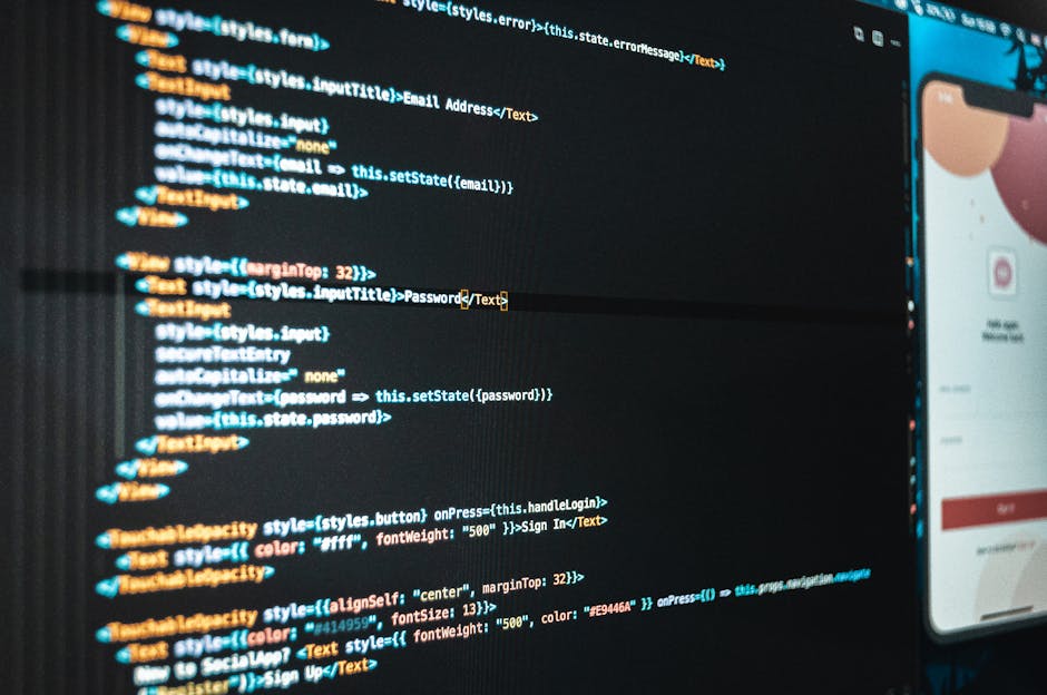 Close-up view of a computer monitor displaying a dark-themed coding interface with lines of HTML and CSS code highlighted in various colors, including blue, orange, and white, on the left side. To the